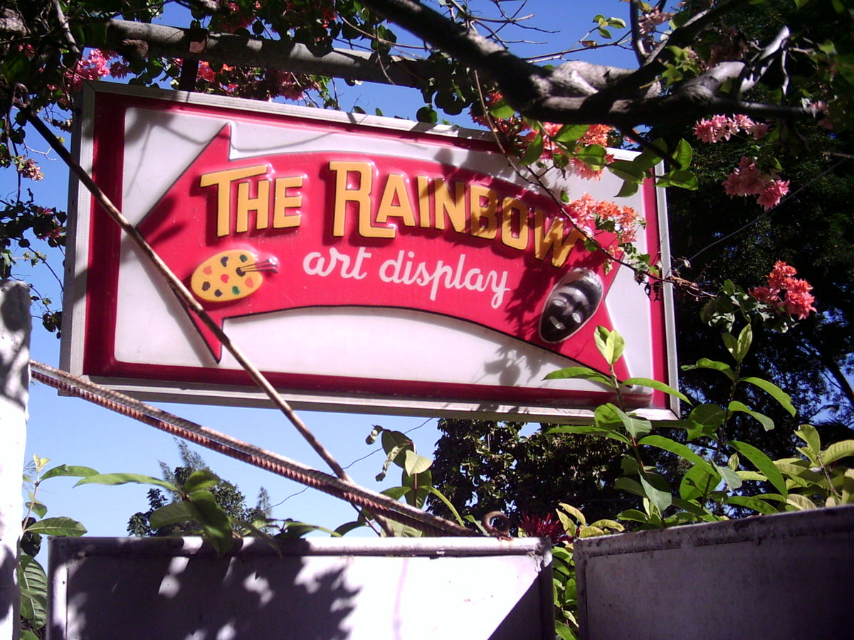 The Rainbow Art Display sign, a red arrow with a painter's palette, under flowering trees