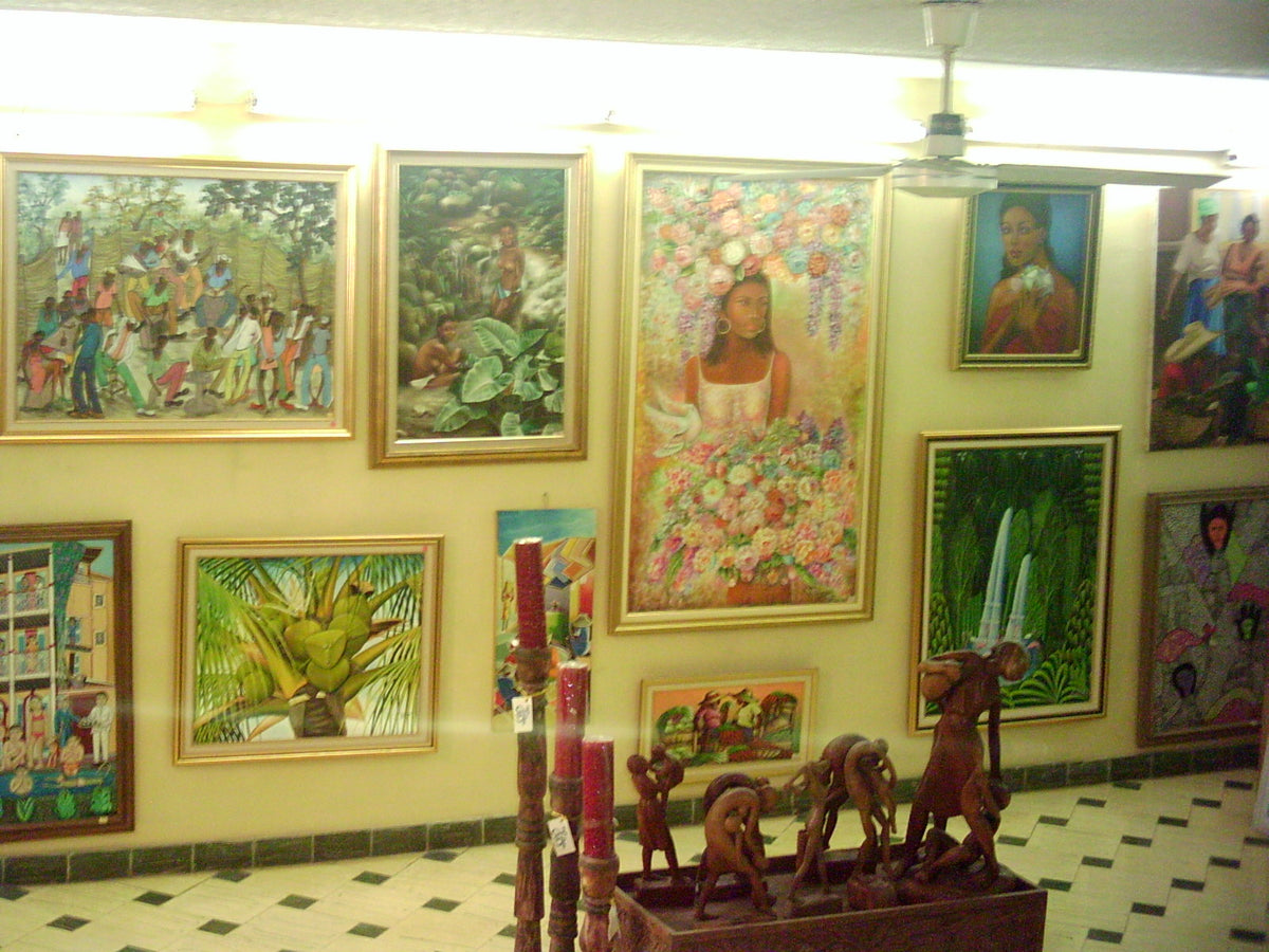 A gallery wall of framed paintings above carved wooden figures and candles